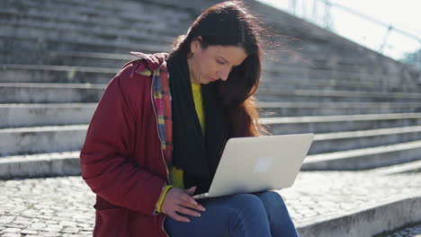 Thoughtful-woman-sitting-on-pavement-with-laptop-on-her-knees